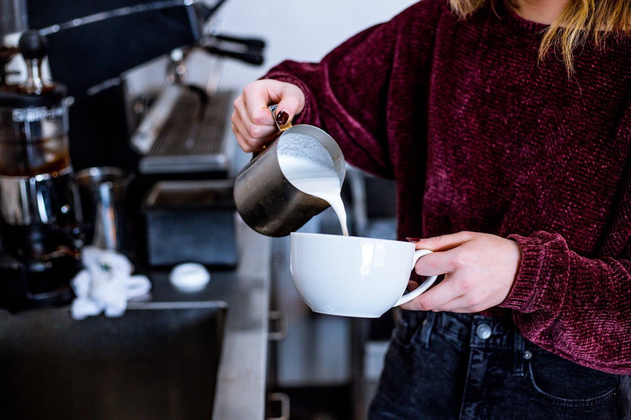 A barista expertly pouring steamed milk into a cup for latte art in a coffee shop.