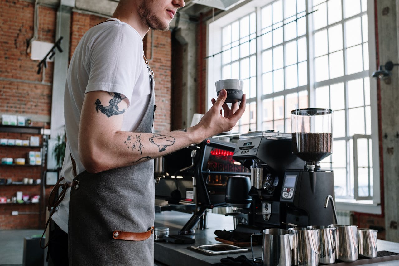 Barista in modern cafe holding coffee cup beside espresso machine, showcasing coffee culture.