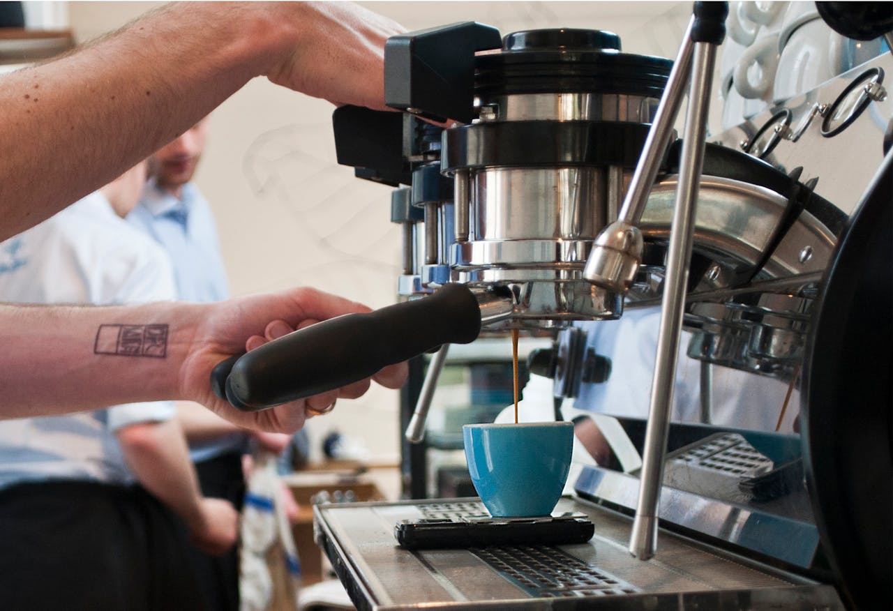 Barista using espresso machine to brew coffee in a café. Hands holding portafilter with focus on ceramic cup.