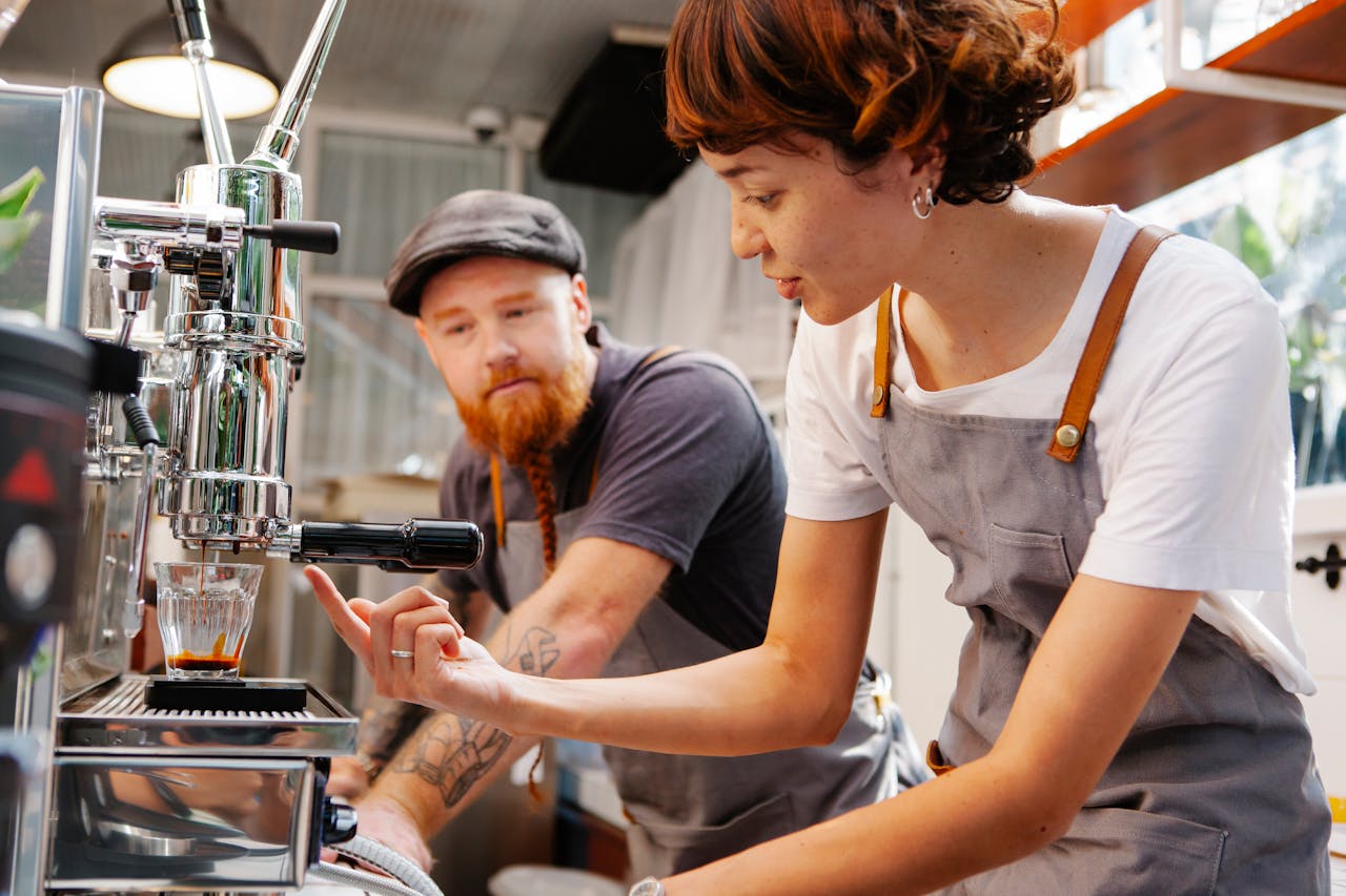 Two baristas making espresso with a professional machine in a cozy café setting.